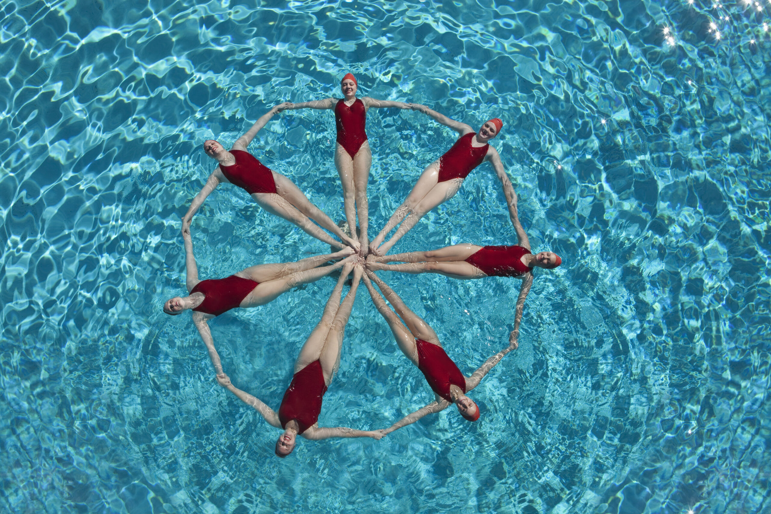Elevated,View,Of,Synchronised,Swimmers,Forming,A,Circle,In,Pool